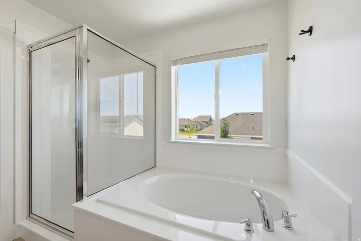 Built-in soaking tub with chrome fixtures, accompanied by a separate glass-enclosed shower
