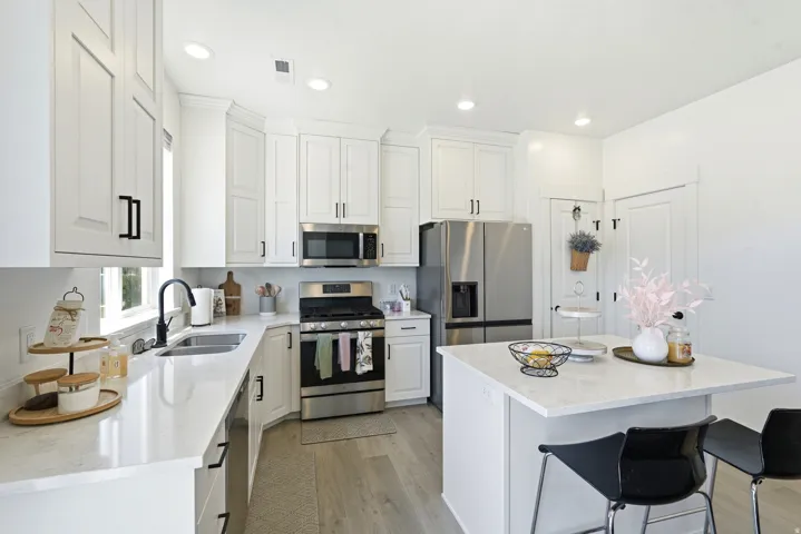 Kitchen featuring white cabinetry with matte black hardware, stainless steel appliances, light-toned countertops, and wood-finish flooring