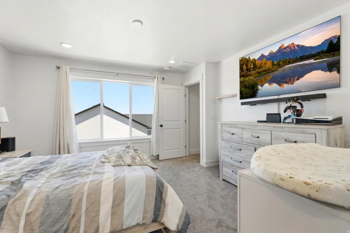 Bright bedroom featuring a large window, recessed lighting, and light gray carpeting