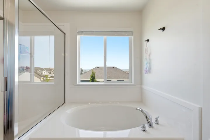 Built-in soaking tub with chrome fixtures, framed by a large window with neighborhood scenery