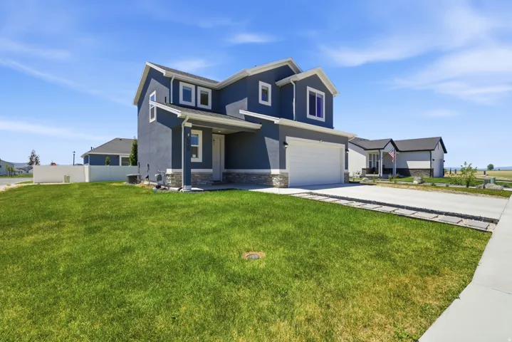 Two-story residence featuring a dark blue exterior with white trim, stone accent detailing, an attached garage, a concrete driveway, and a manicured lawn