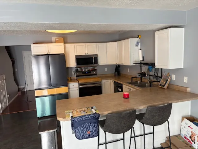 U-shaped kitchen featuring white cabinetry, light-toned countertops, and stainless steel appliances including a microwave, range, and sink