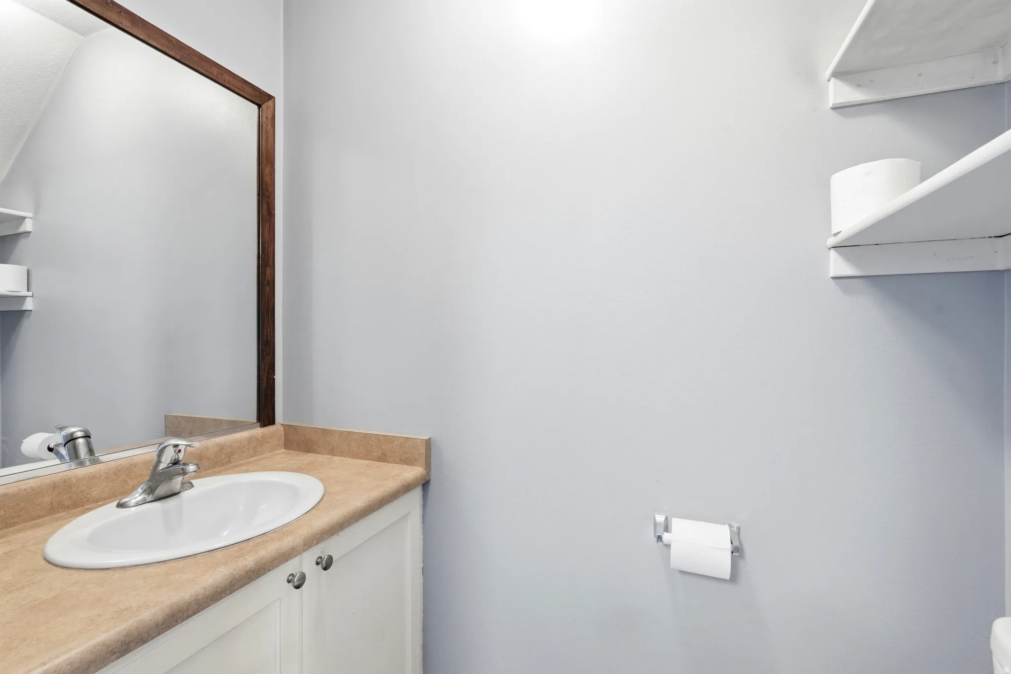 Bathroom vanity featuring an oval sink, chrome faucet, and a mirror with a wood-finish frame