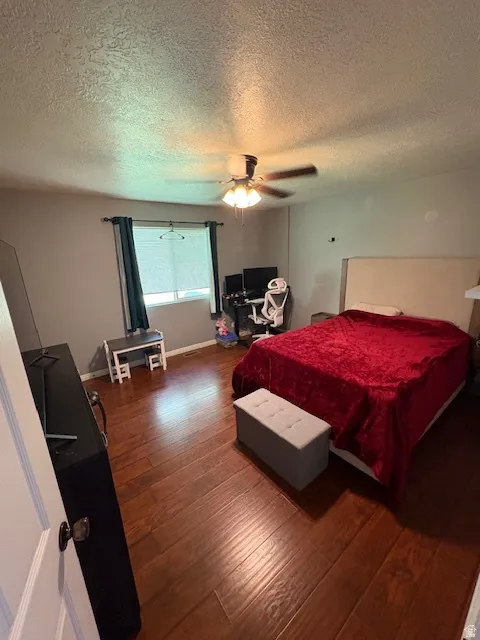 Bedroom featuring wood-finish flooring, a ceiling fan, window with blinds and dark curtains, and a light-colored headboard