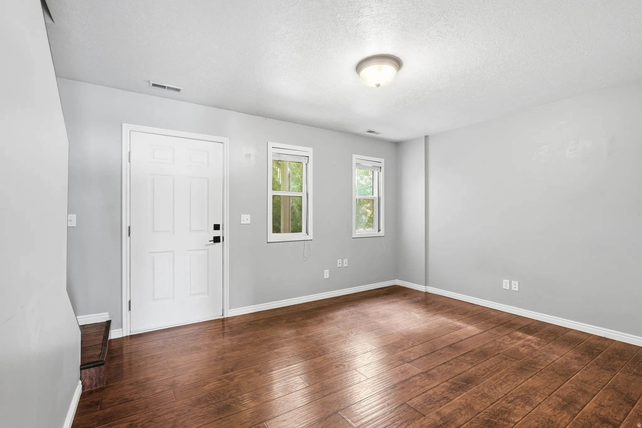 Spacious room featuring wood-finish flooring, light gray walls, white trim, and a contemporary ceiling light fixture