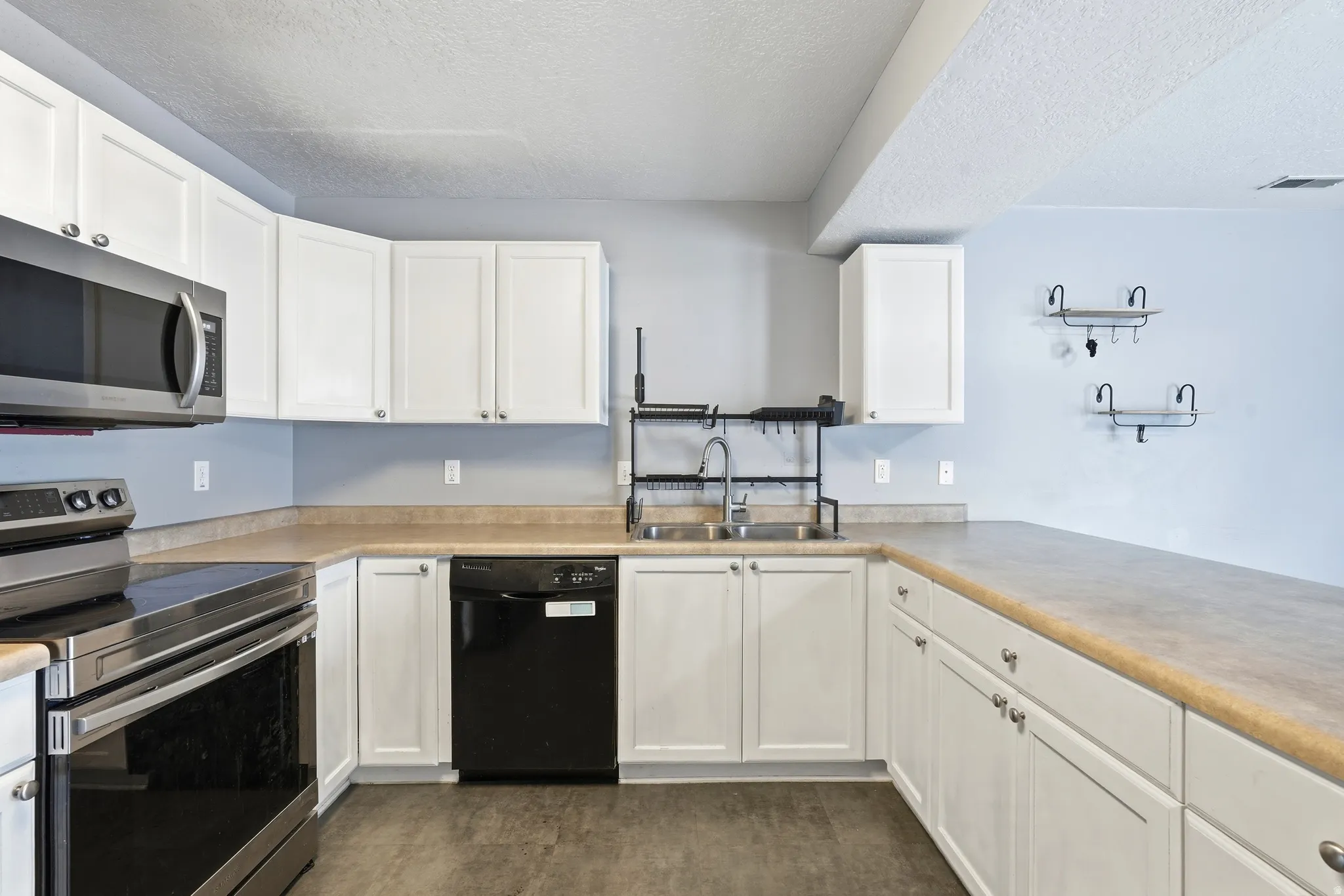 Kitchen featuring white cabinetry, light countertops, stainless steel microwave, black dishwasher, and a stainless steel range