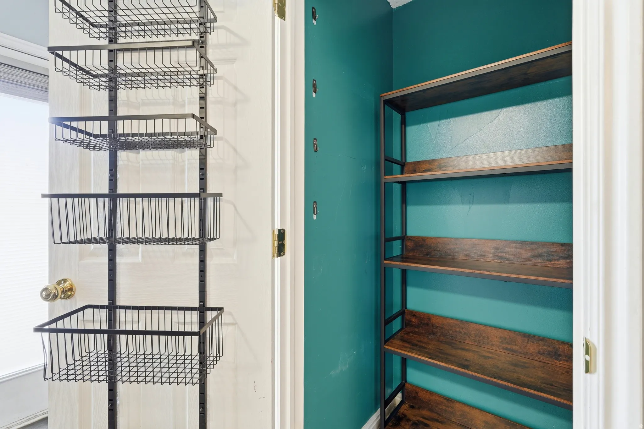 Interior storage area featuring a vivid teal wall, a four-tier wood-finish shelving unit, and an organizing system with multiple wire baskets