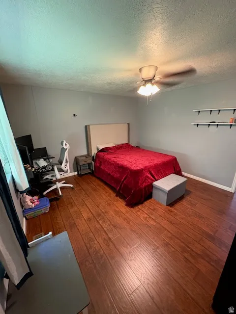 Spacious room featuring wood-finish flooring, a ceiling fan with integrated lighting, and wall-mounted shelving