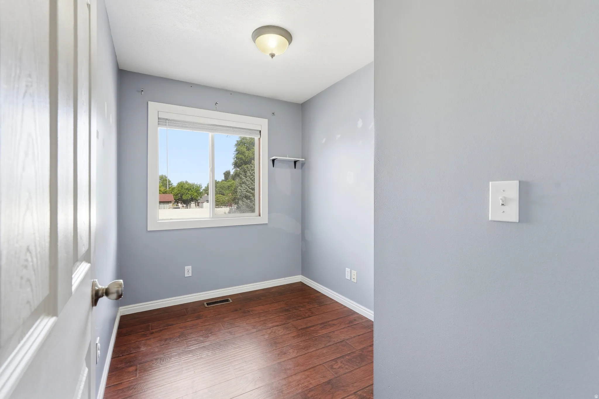 Room featuring a single window, wood-finish flooring, and a ceiling-mounted light fixture