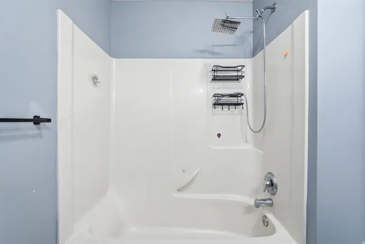Bathtub and shower combination featuring a square rainfall showerhead, handheld shower fixture, and polished chrome hardware