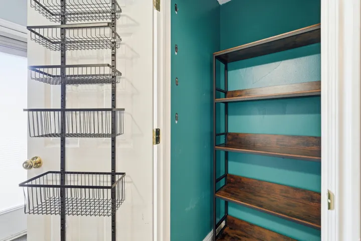 Interior storage area featuring a vivid teal wall, a four-tier wood-finish shelving unit, and an organizing system with multiple wire baskets