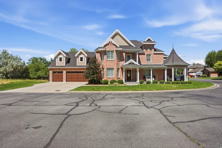 Brick facade residence featuring a covered front porch, a circular gazebo, two prominent dormers, and an attached two-car garage with wood-finish doors