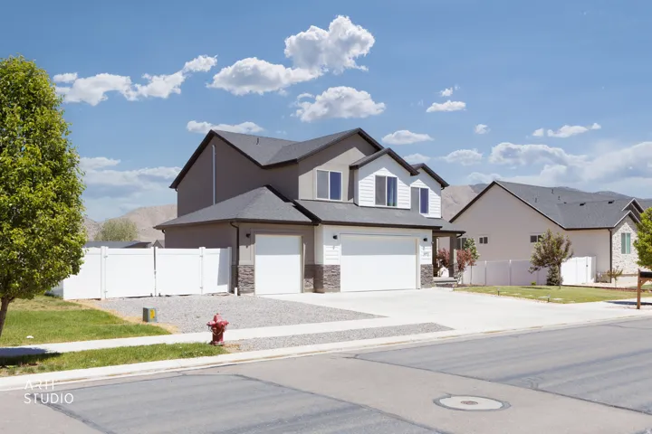 Two-story residence featuring a gray exterior with white siding accents, a dark shingle roof, and a two-car garage with stone veneer details