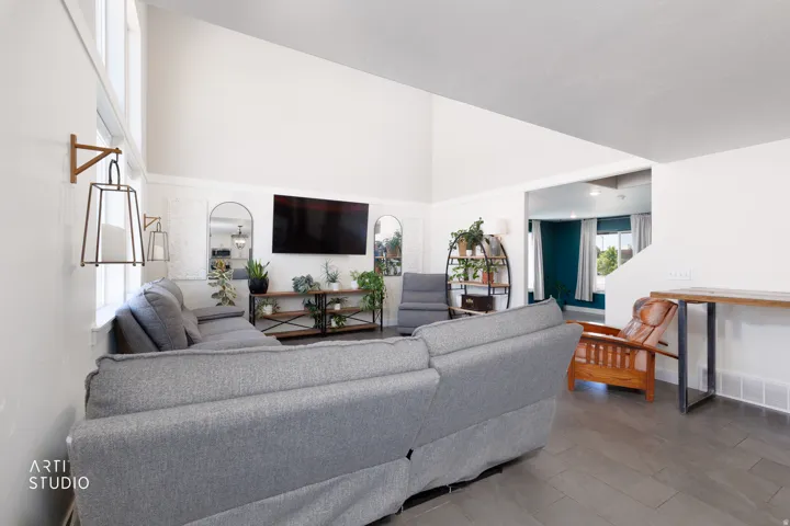 Spacious living area featuring vaulted ceilings, a wall of high windows, contemporary wall sconces, wood-finish flooring, and recessed lighting