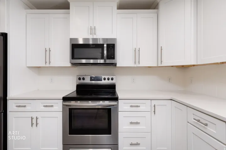 Modern kitchen featuring white shaker cabinetry, stainless steel appliances, light-toned countertops, and a full suite of upper and lower storage