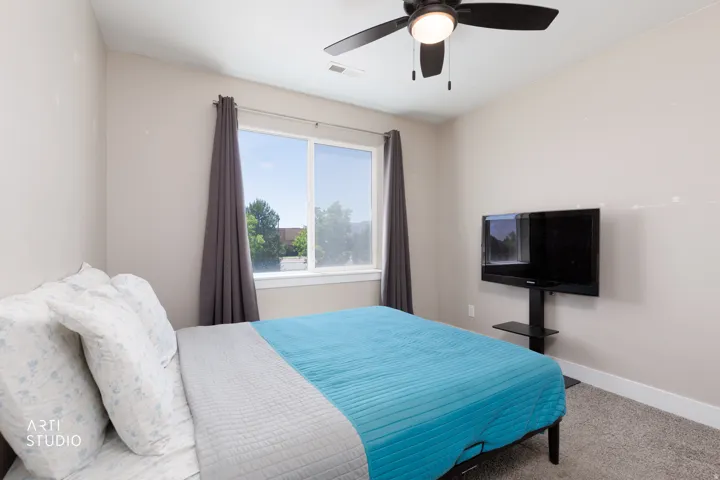 Carpeted room featuring a ceiling fan with integrated lighting, a window with curtains, and a wall-mounted TV stand