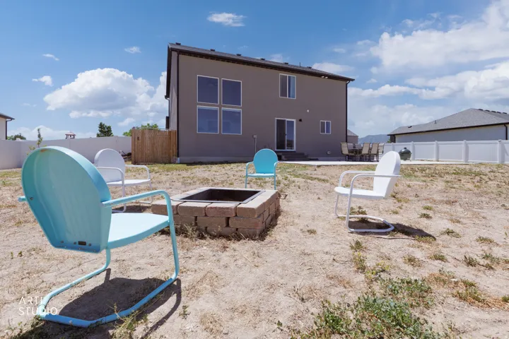 Expansive backyard featuring a built-in fire pit with brick surround, a concrete patio, and a white vinyl privacy fence