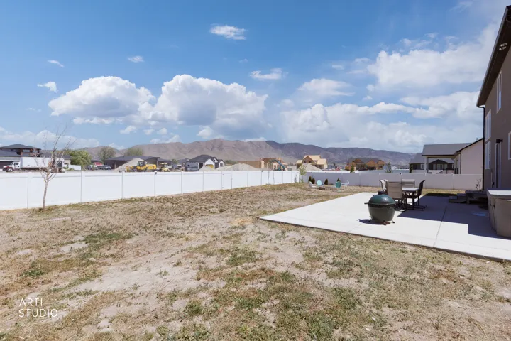 Spacious backyard featuring a concrete patio, white privacy fencing, and mountain scenery