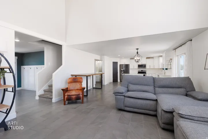 Spacious open-concept living area featuring large format tile flooring, a staircase with carpeted treads, and a white paneled entryway with hooks