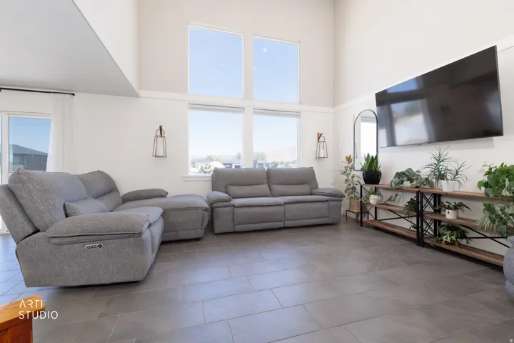 Spacious living area featuring high ceilings, large windows, tile flooring, and decorative wall sconces