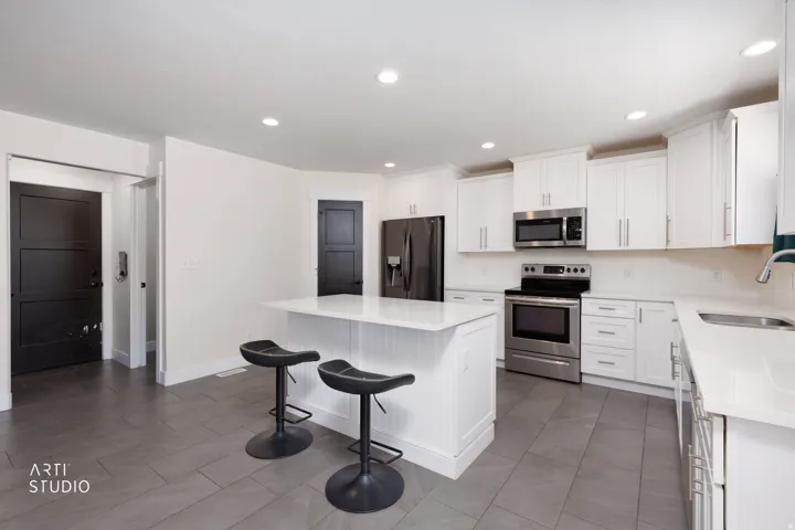 Modern kitchen featuring a central island with white beadboard paneling, white countertops, stainless steel appliances, white cabinetry, and large format tile flooring