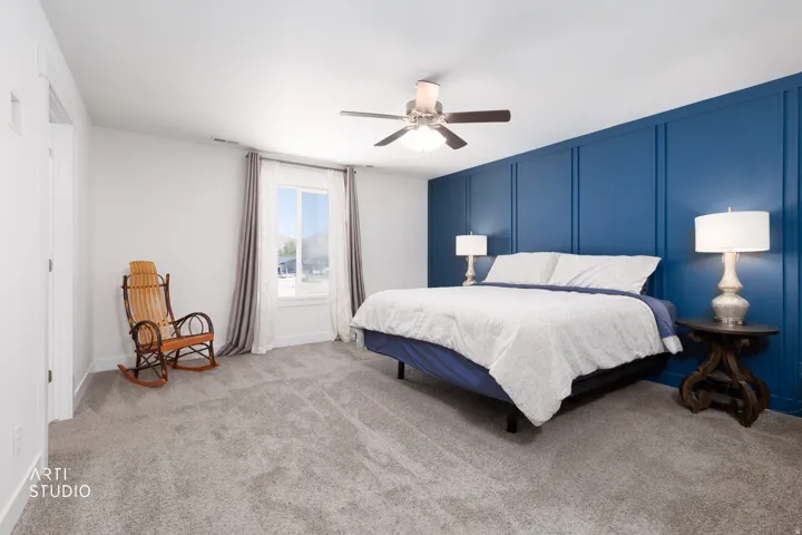 Spacious bedroom featuring an accent wall with board and batten detailing, light gray carpeting, and a ceiling fan with integrated lighting