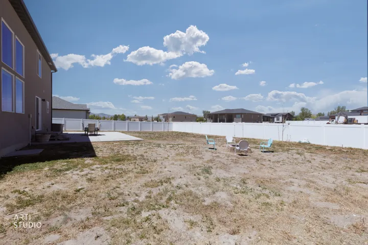 Expansive backyard with a large concrete patio, a full privacy fence, and undeveloped terrain
