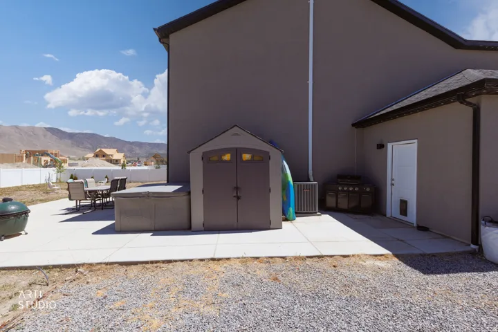 Expansive concrete patio area with a storage shed and white vinyl fencing