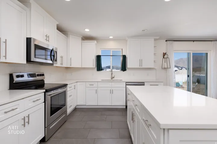 Bright kitchen featuring white shaker cabinetry, stainless steel appliances, white countertops, and dark tile flooring