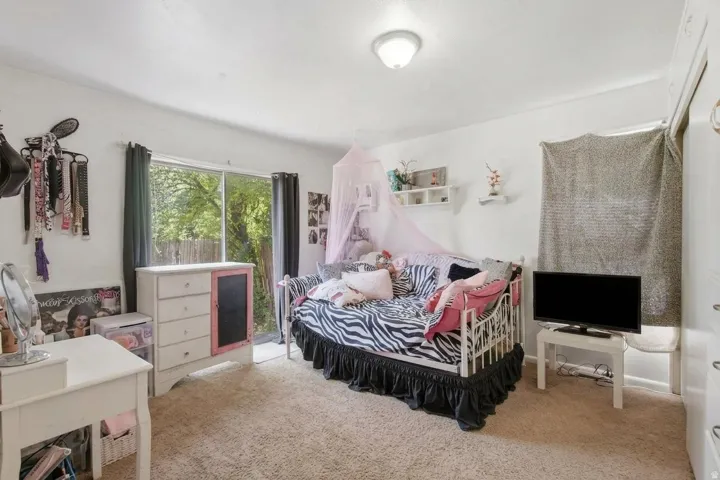Carpeted room with white walls, featuring a sliding glass door with dark curtains, a built-in flush-mount ceiling light fixture, and shelving
