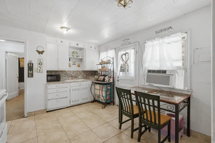 Kitchen area featuring tile flooring, white cabinetry, a single basin sink, and a window unit