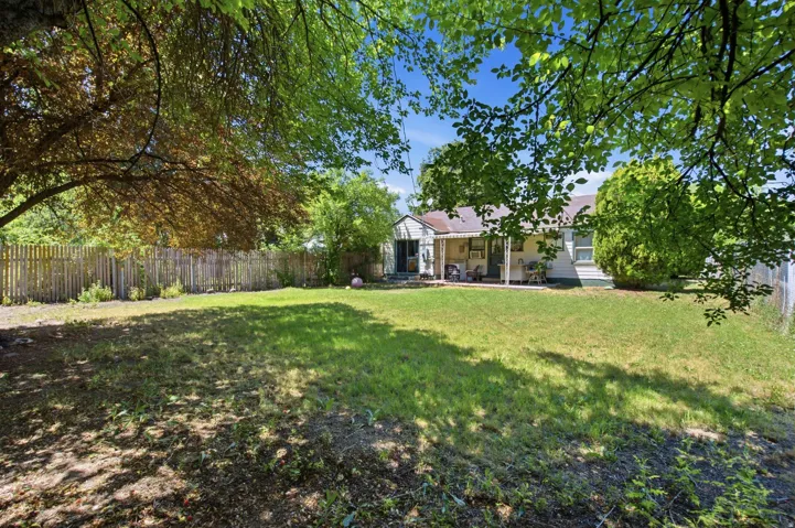 Expansive backyard featuring a large lawn area, mature trees providing shade, and a wood picket fence