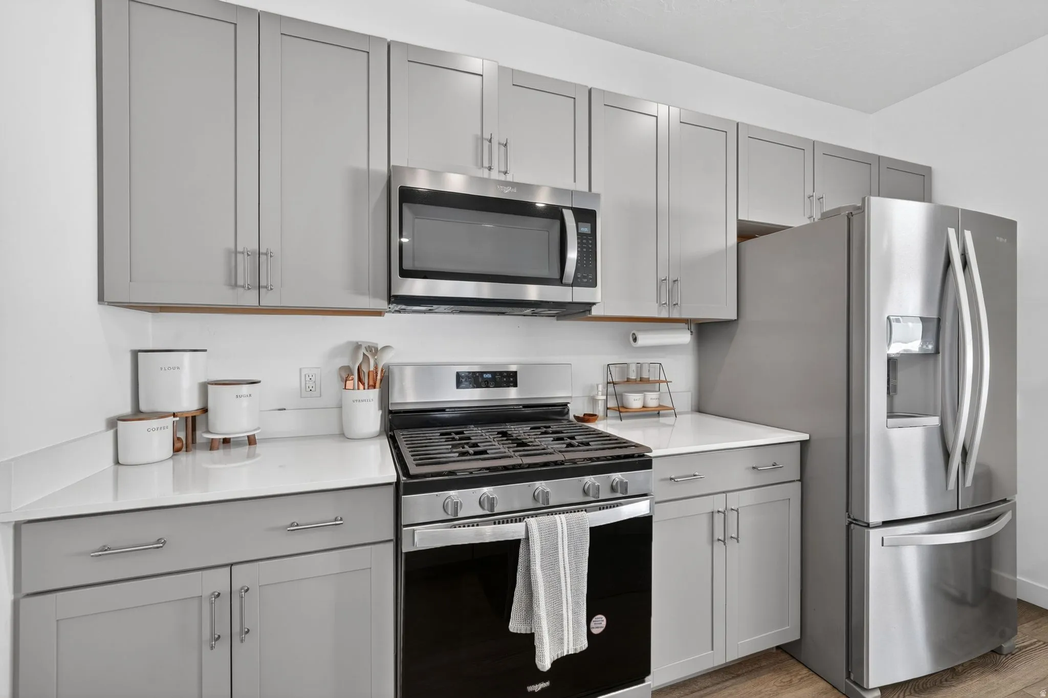 Contemporary kitchen featuring light gray cabinetry, stainless steel appliances, white countertops, and wood-finish flooring