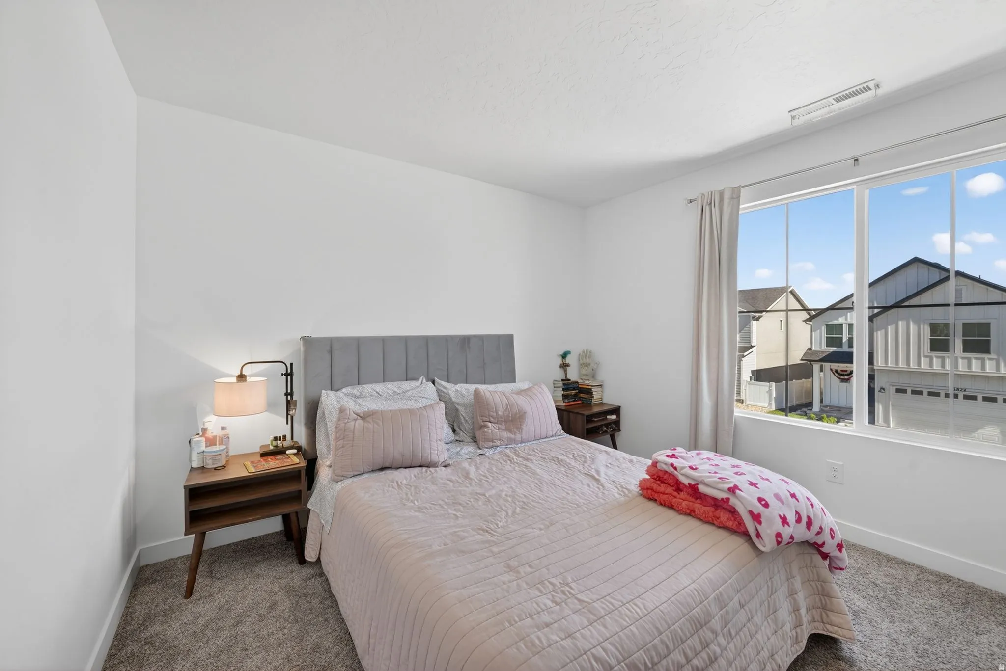 Bright bedroom featuring a large window, plush carpet flooring, and white walls