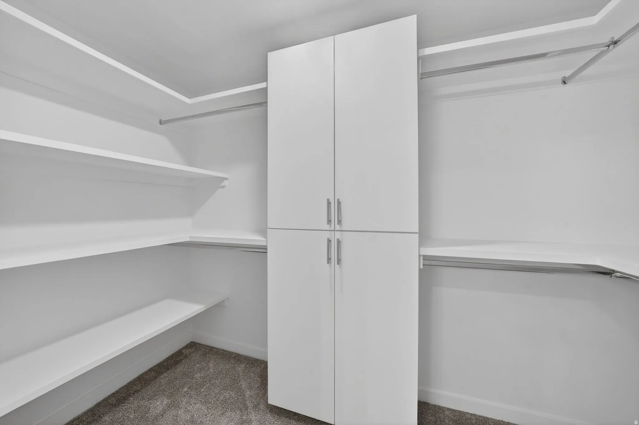 Walk-in closet featuring white built-in shelving, hanging rods, and a central storage cabinet with brushed metal hardware