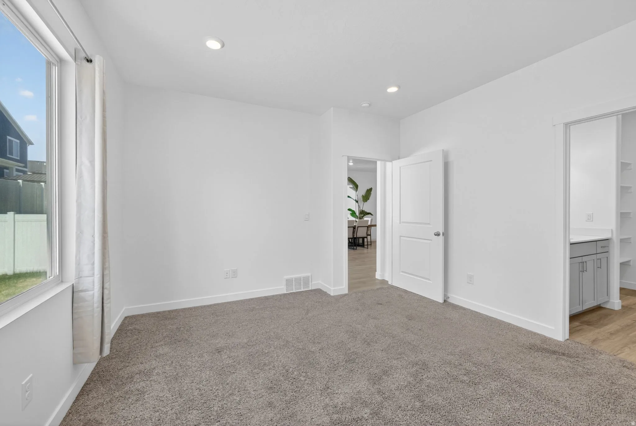 Neutral-toned carpeting throughout this room, featuring recessed lighting, white walls, and a large window