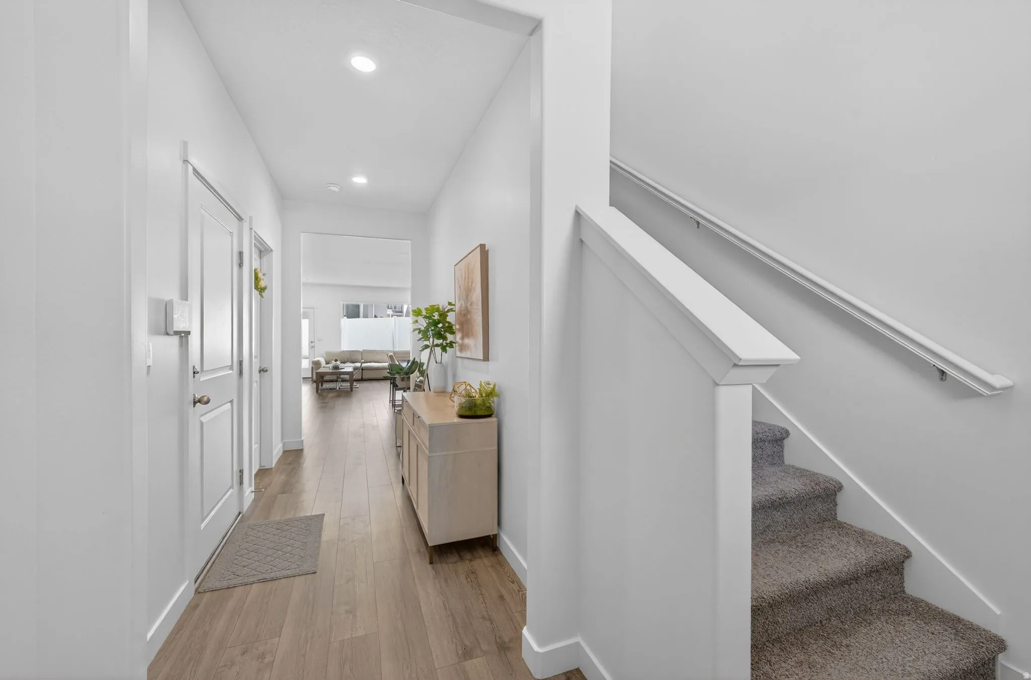 Hallway featuring wood-finish flooring, recessed lighting, white trim, and a carpeted staircase with a white handrail