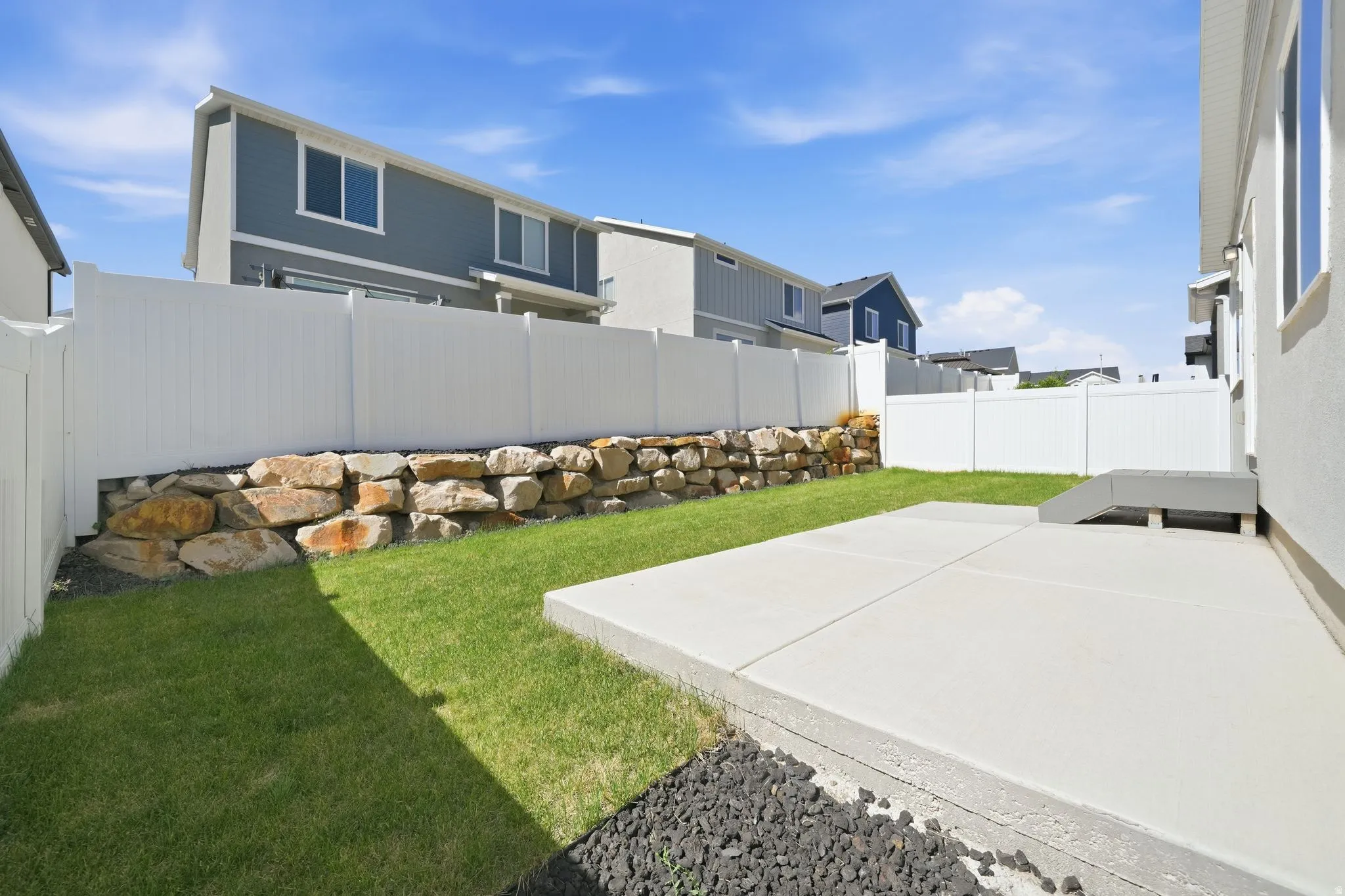 Private backyard with a concrete patio, green lawn, and a stone retaining wall