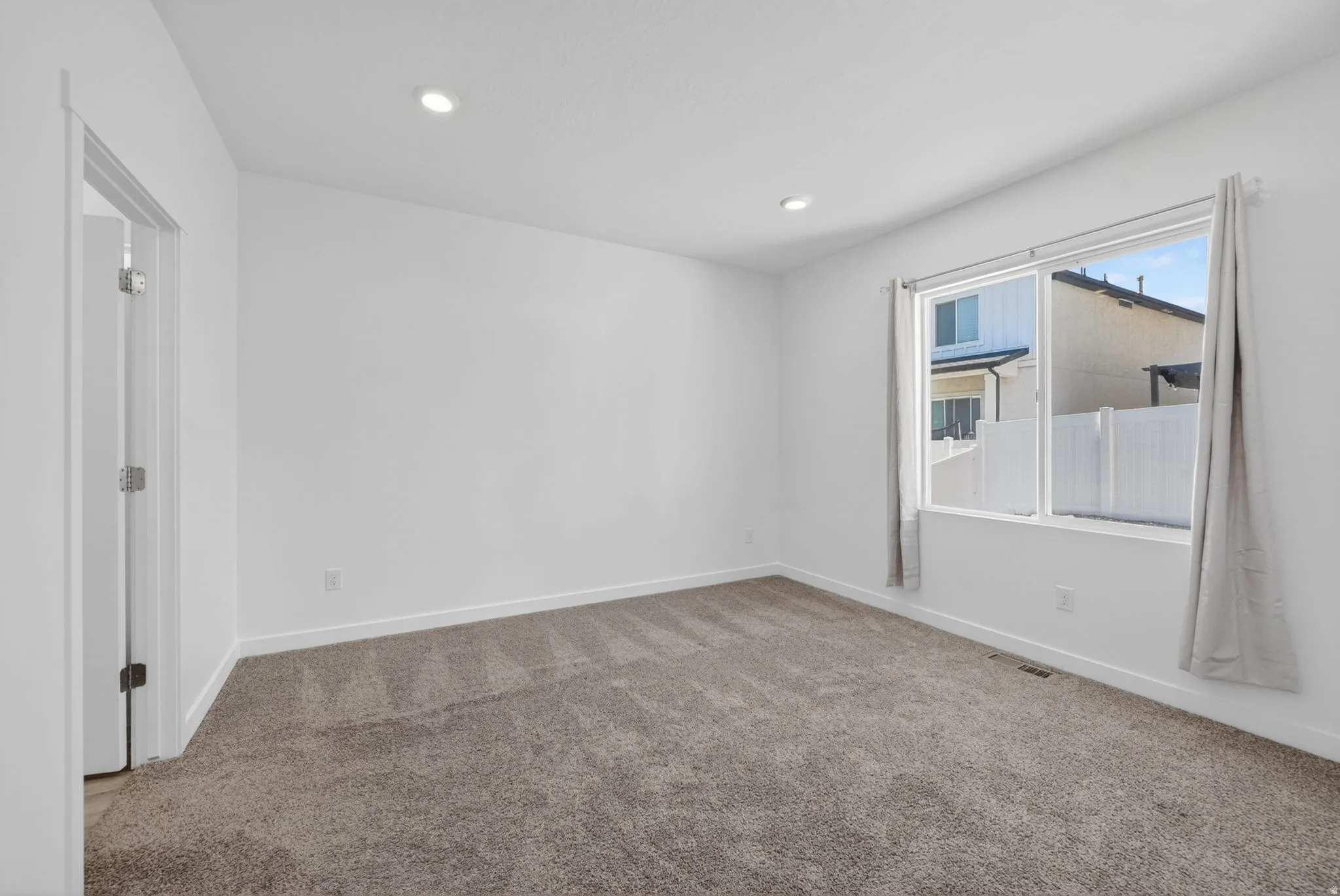 Spacious room featuring neutral carpeting, white walls, recessed ceiling lighting, and a large window with white framing