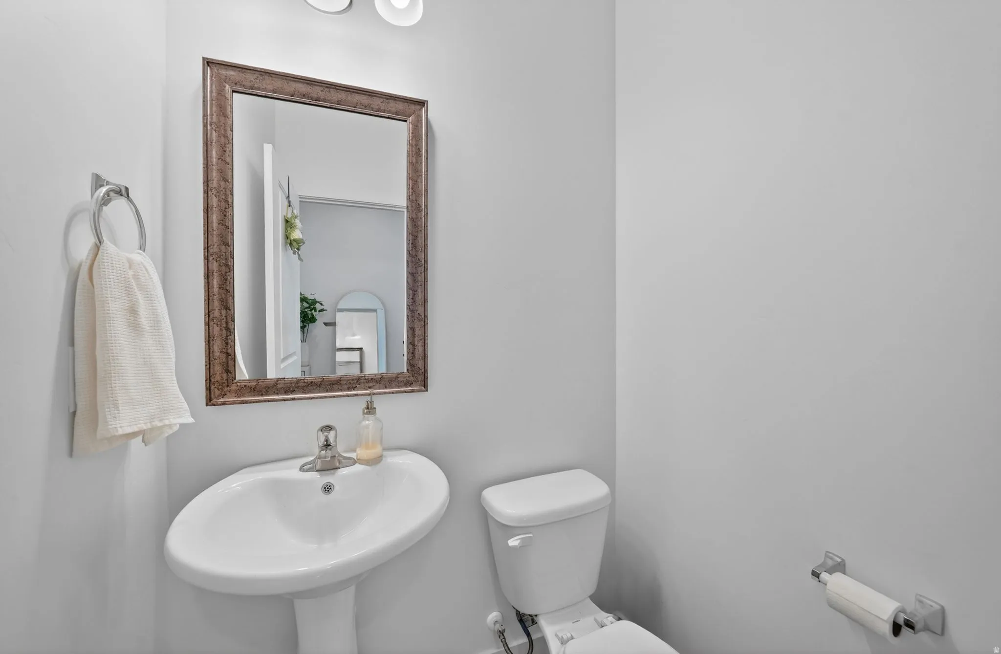 Pedestal sink with chrome faucet, framed mirror, and wall-mounted lighting