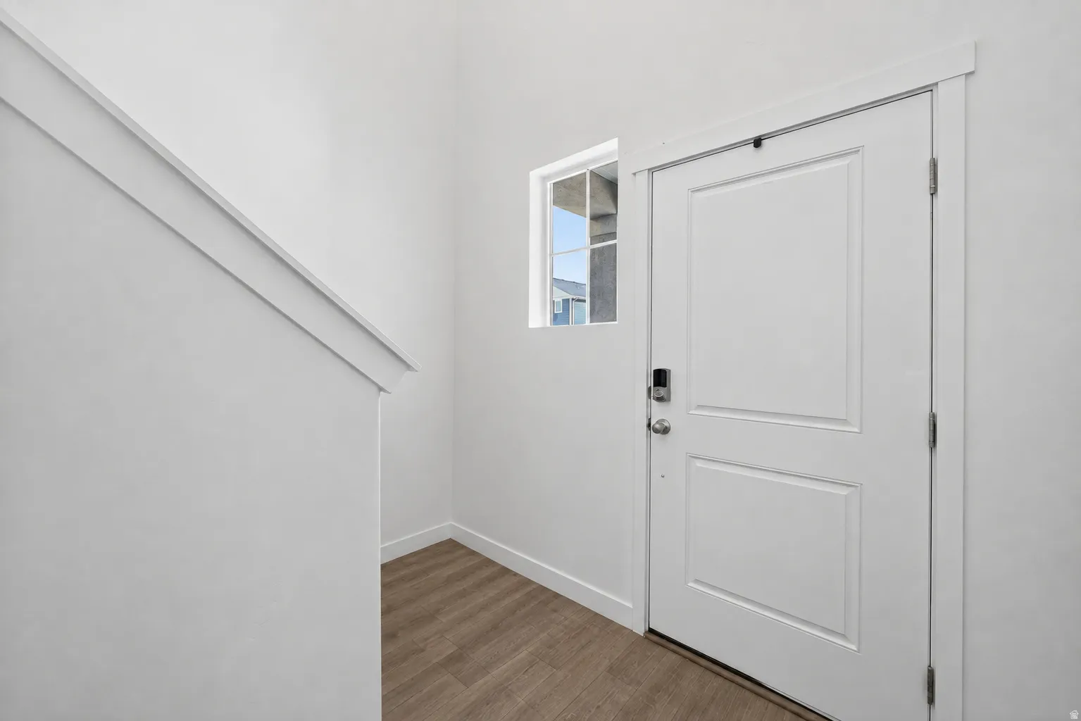 White paneled door with smart lock entry, wood-finish flooring, and white baseboards
