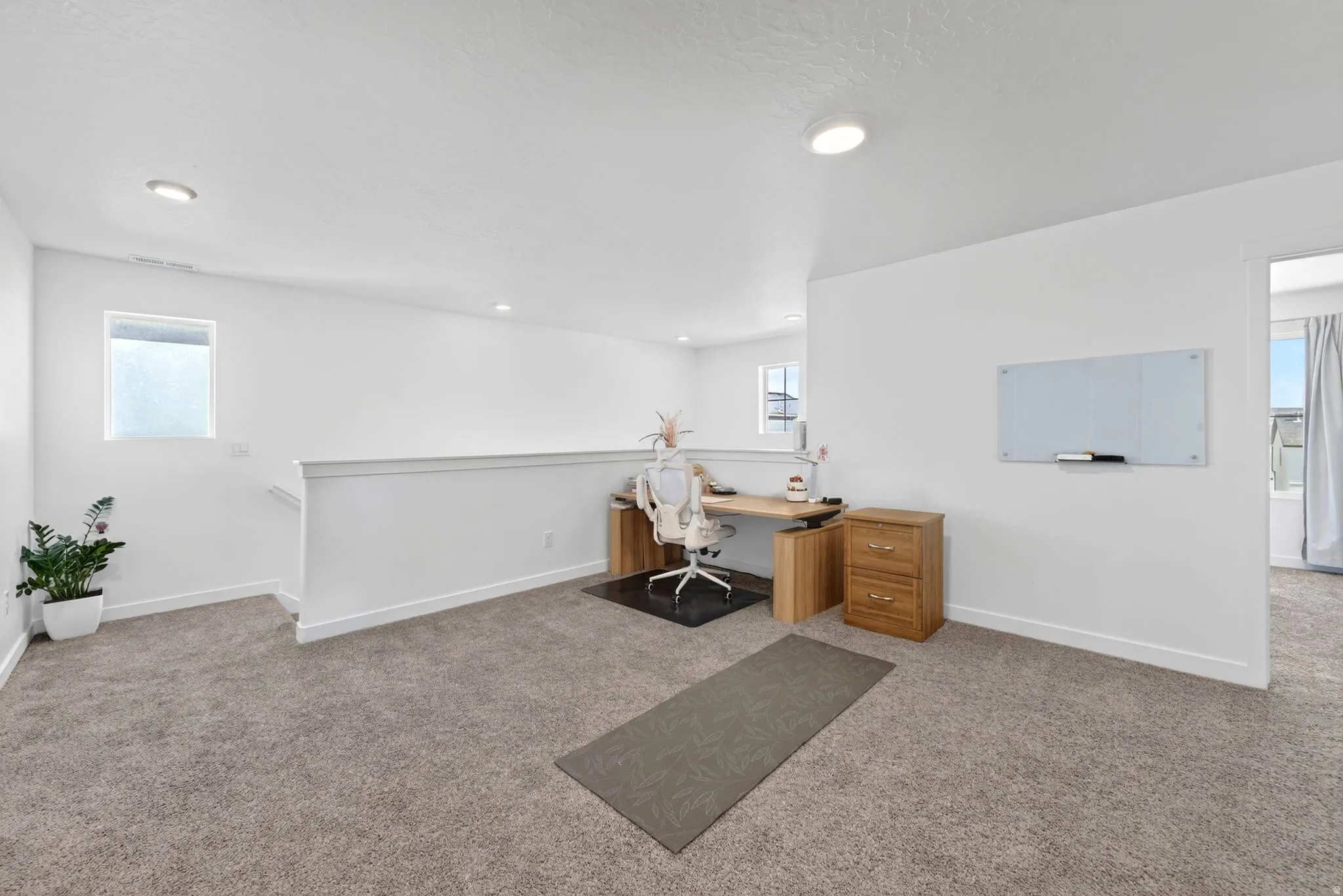 Spacious loft area featuring neutral-toned carpeting, recessed lighting, a half-wall partition, and a frosted window providing natural light