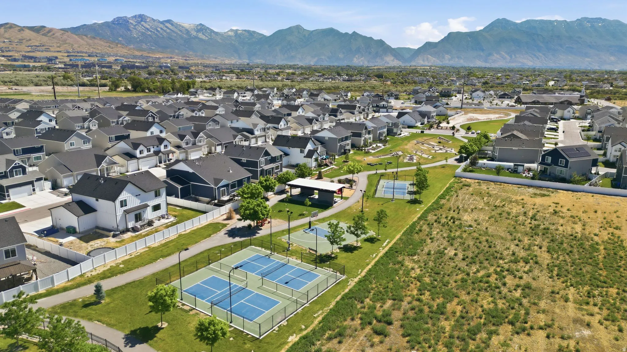 Aerial perspective showcasing a residential community with contemporary homes, mountain backdrop, and multiple recreational courts