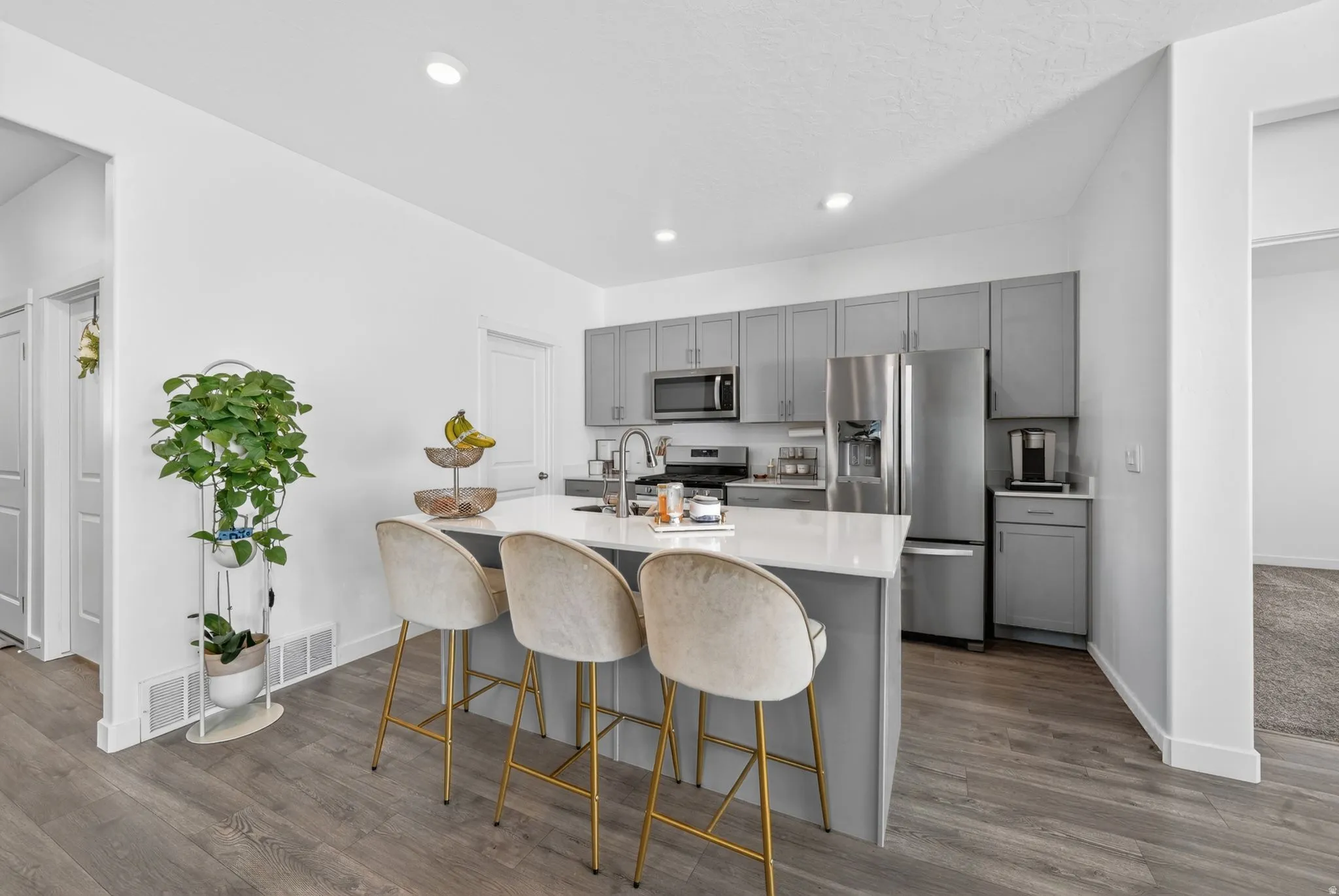 Spacious kitchen featuring an island with countertop seating, stainless steel appliances, gray cabinetry, recessed lighting, and wood-finish flooring