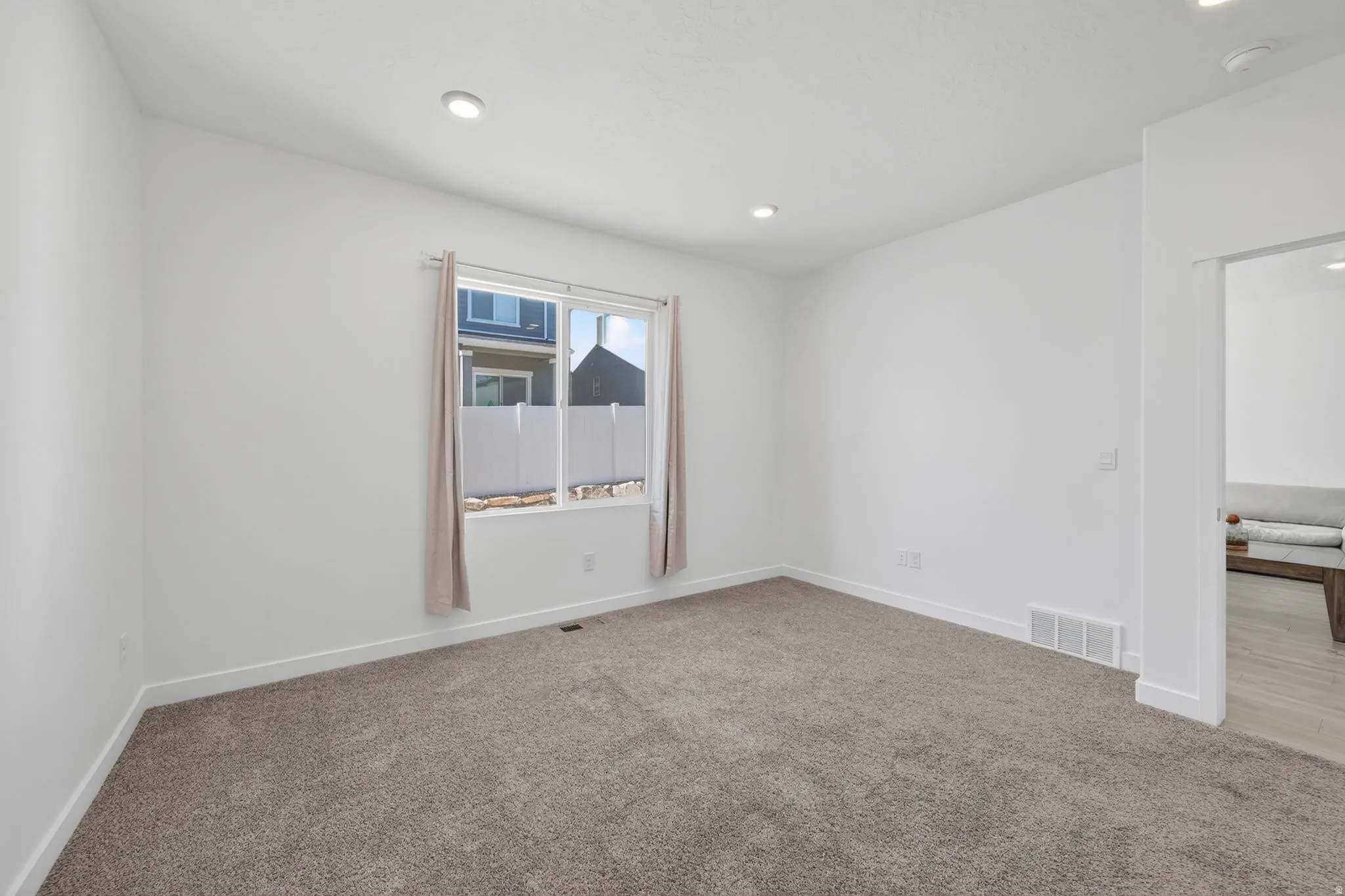 Spacious room featuring neutral carpeting, white walls, recessed ceiling lighting, a large window, and white baseboards
