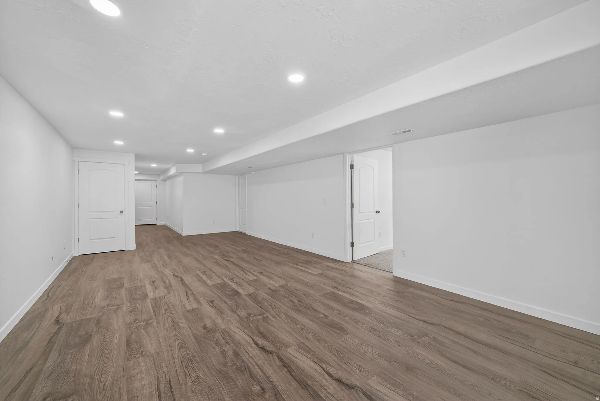Spacious room featuring wood-finish flooring, white walls, multiple recessed lights, and white paneled doors