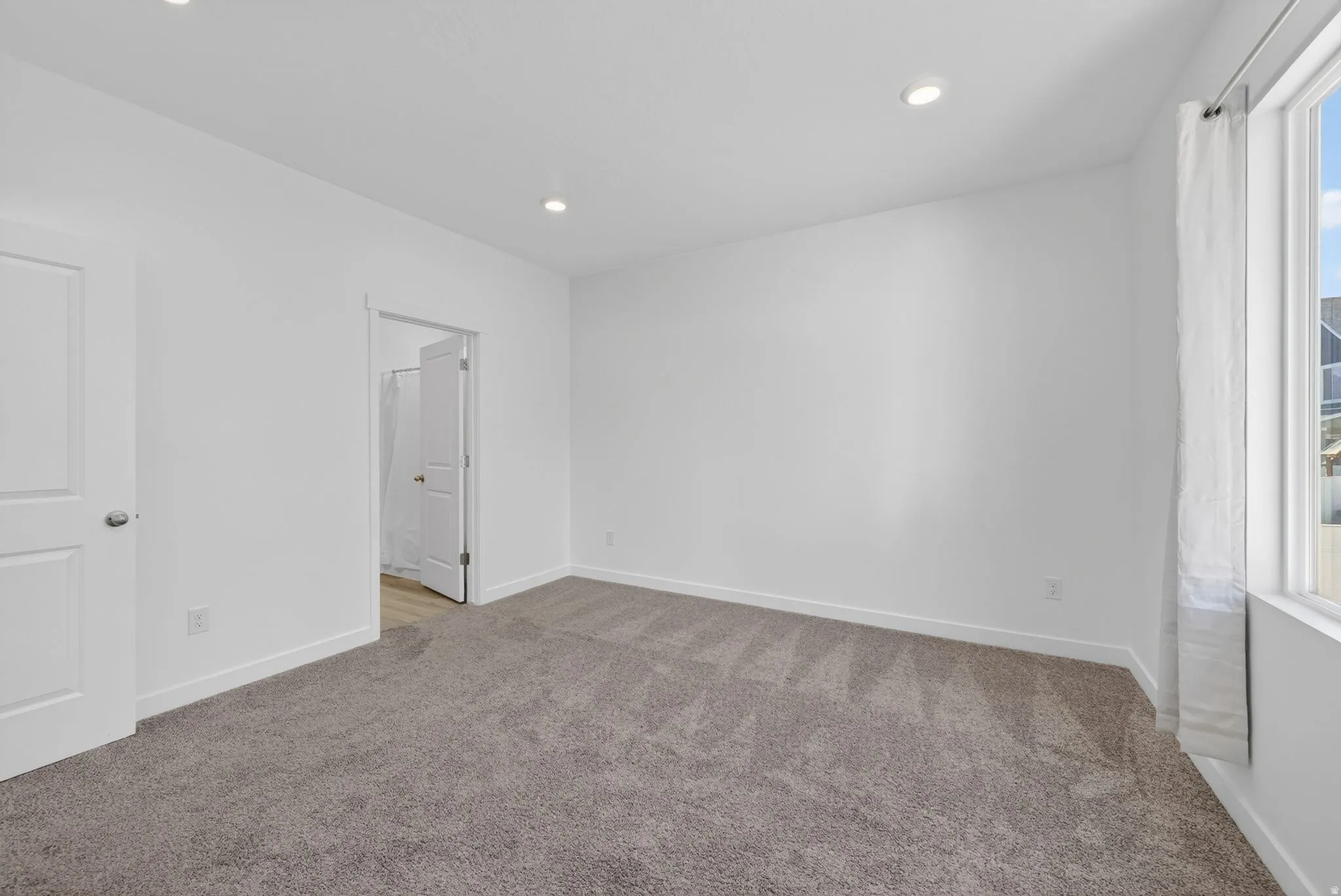 Spacious room featuring gray carpet, recessed lighting, white walls, and a large window