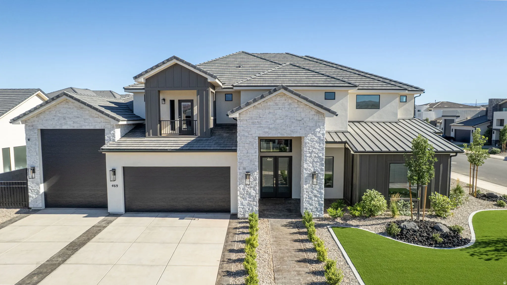 Modern exterior featuring white stucco, stacked stone accents, a dark metal roof, and a prominent entry with double glass doors