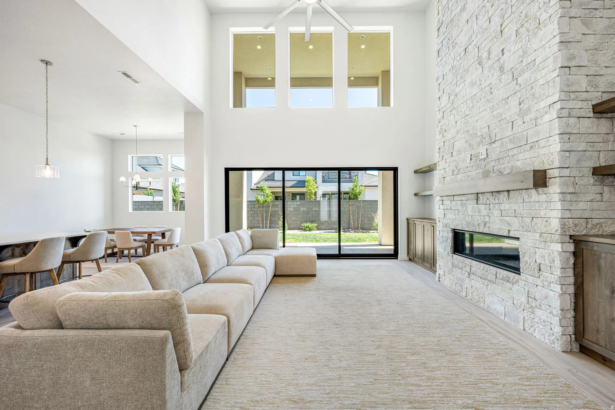 Spacious great room featuring a floor-to-ceiling stone fireplace with an integrated linear firebox, two-story ceilings, and ample natural light from large windows