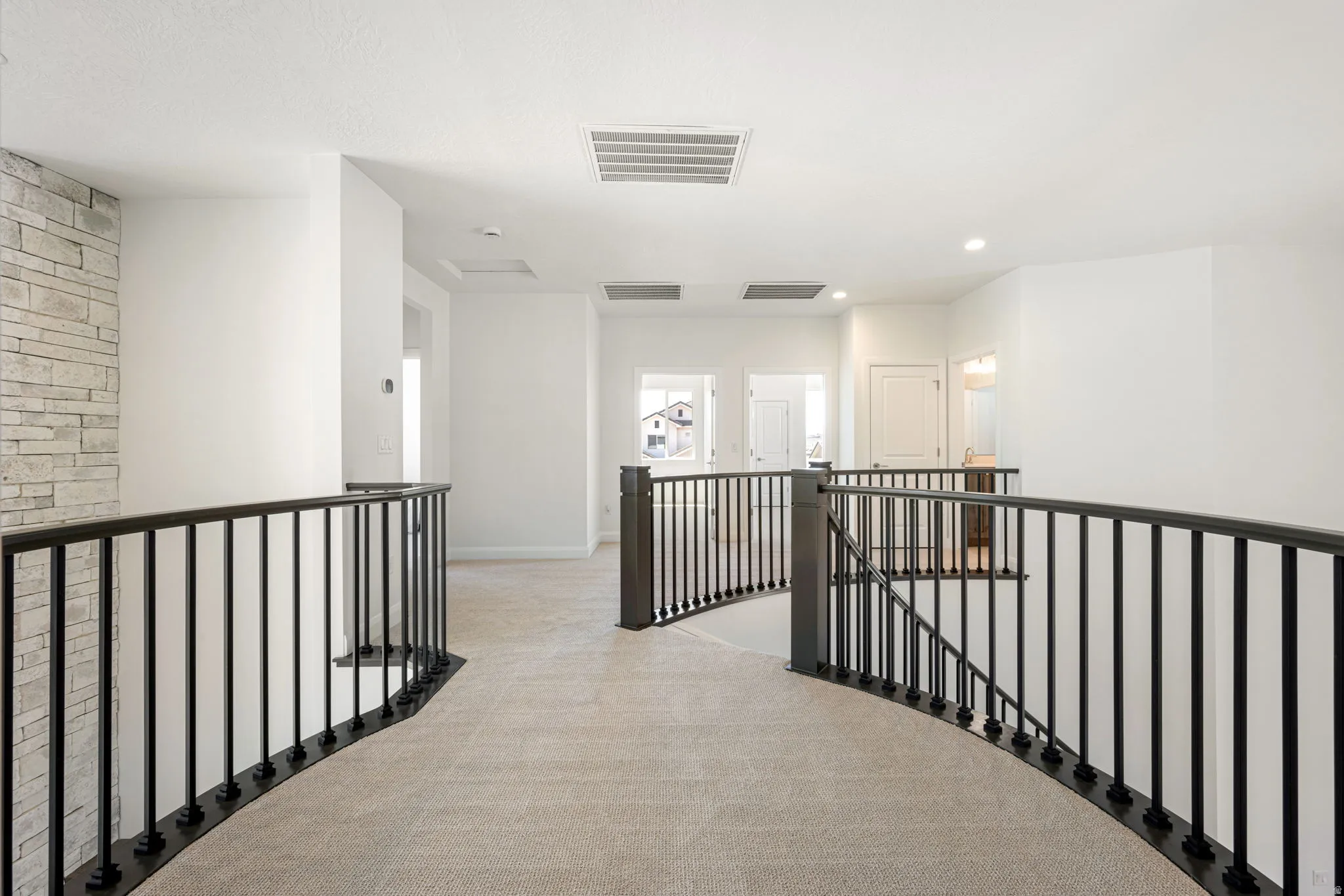 Curved black metal balusters with dark wood-finish newel posts, light neutral carpeting, and a stone-clad accent wall